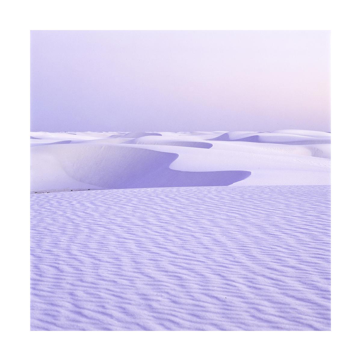 A desert landscape shows sand dunes with shadows and ripples in the sand.