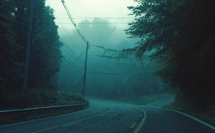 A winding road with a yellow dividing line disappears into a hazy, tree-lined distance.