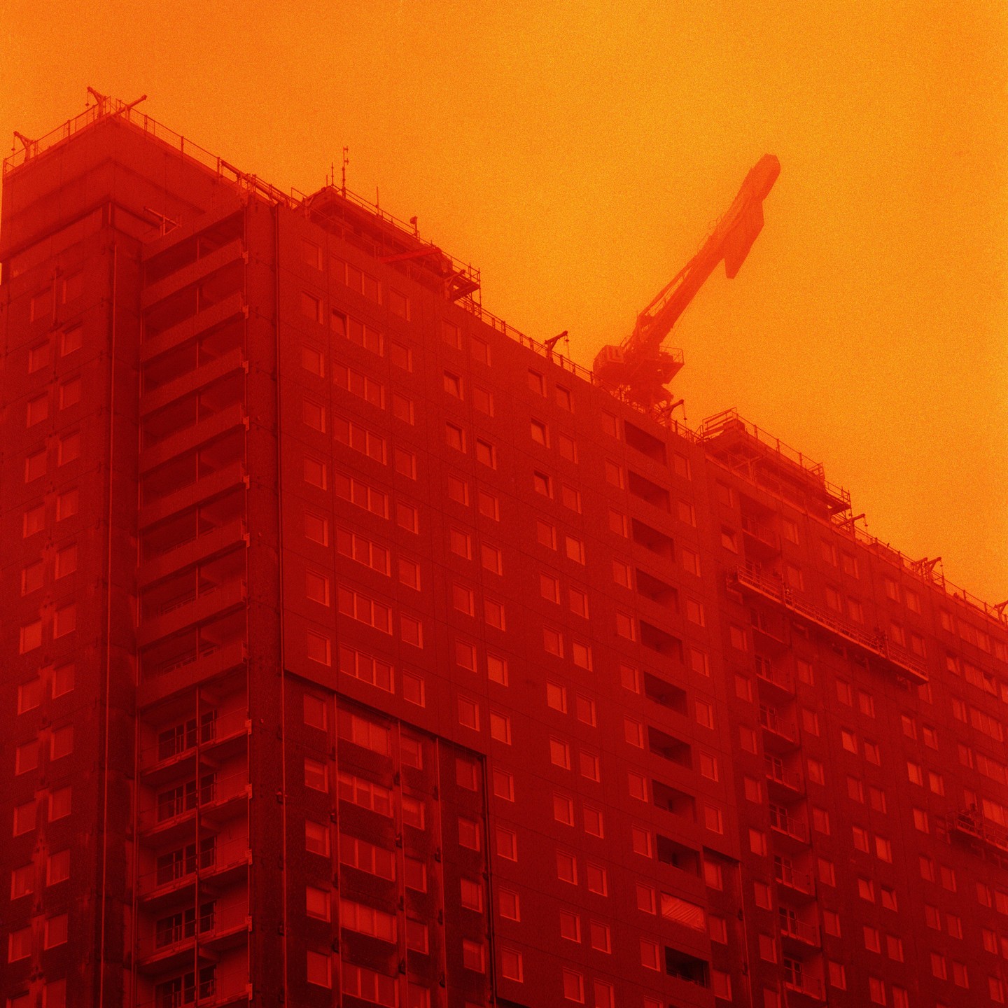A tall building under construction with a crane on top is bathed in a red and orange hue.