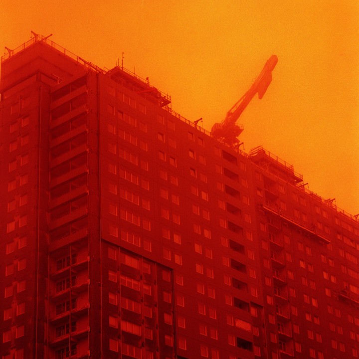 A tall building under construction with a crane on top is bathed in a red and orange hue.