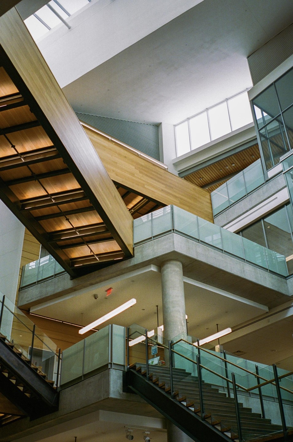 A modern building interior features multiple levels with stairs, glass railings, and wooden architectural elements.