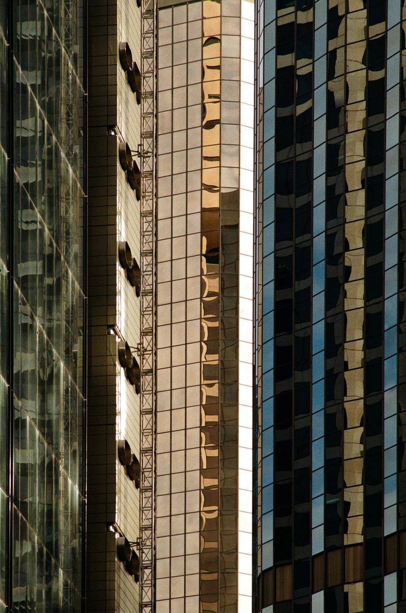 The glass facade of a modern building reflects the sky and other structures.