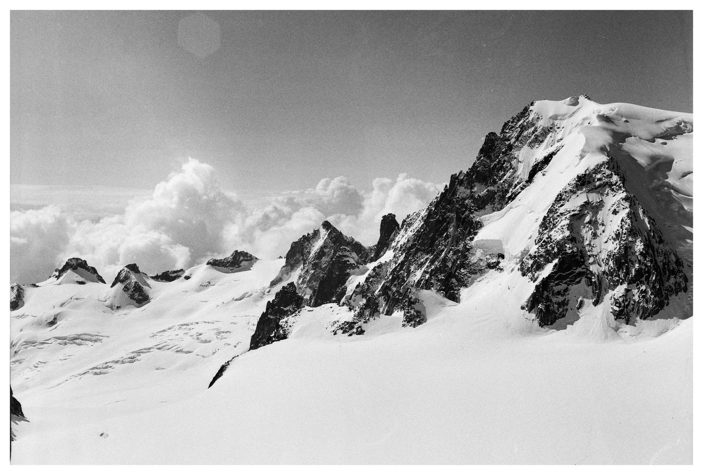 A black and white landscape shows a snow-covered mountain range with clouds in the background.