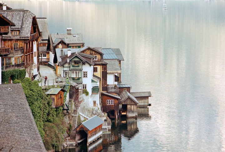 A village with houses and boathouses built into a steep hillside next to a lake.