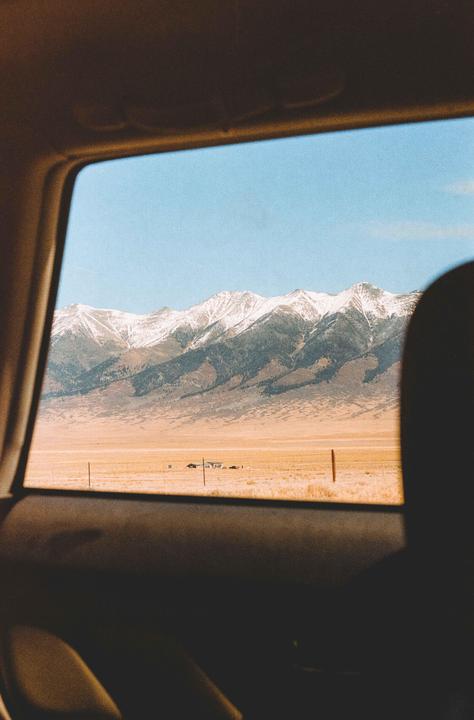 A view from inside a vehicle shows snow-capped mountains in the distance beyond a vast, dry plain.