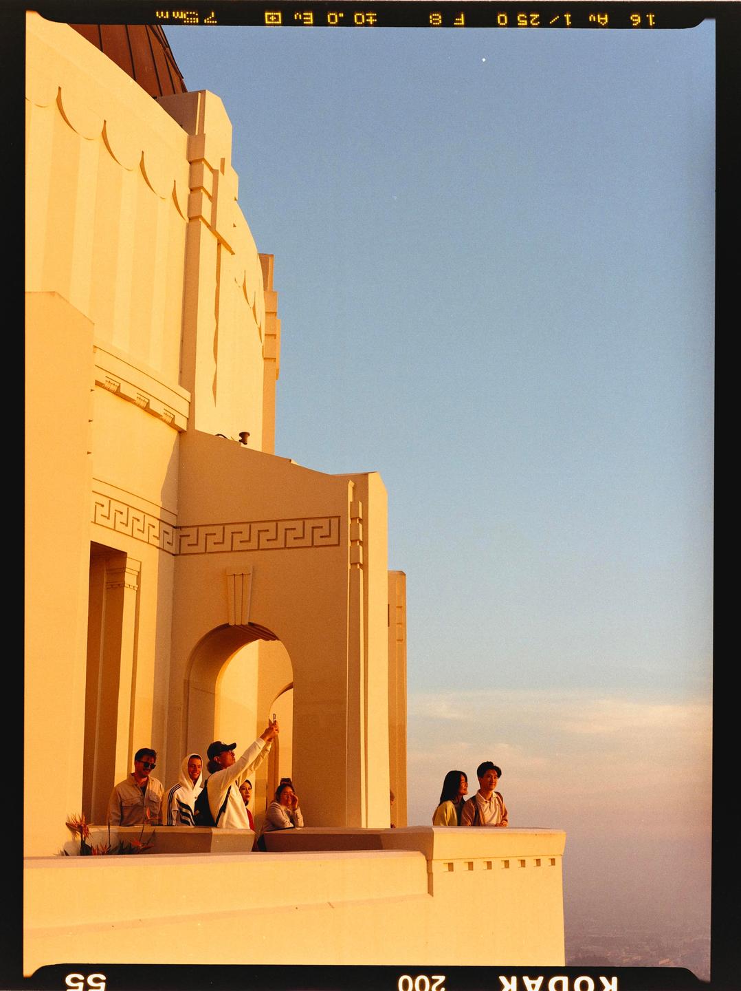 A group of people stand on a balcony of a large building with a clear sky above them.
