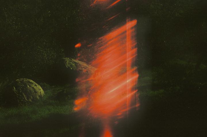 A bright orange light streak illuminates a dark landscape with rocks and grass.