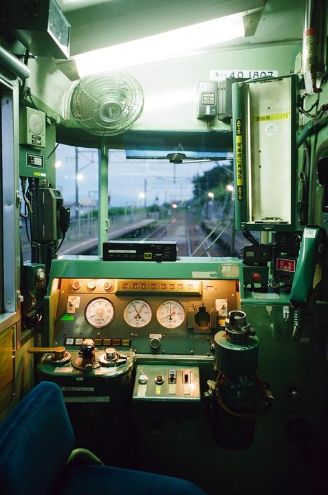 The interior of a train's cockpit is visible, with gauges and controls in the foreground and tracks stretching into the distance through the front window.