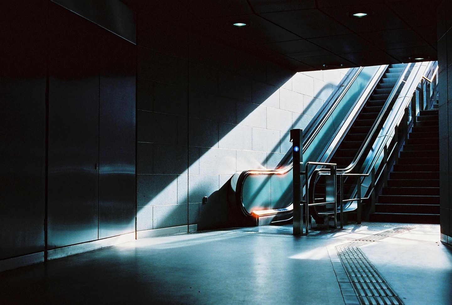 Sunlight illuminates an escalator and a staircase in a subway station.