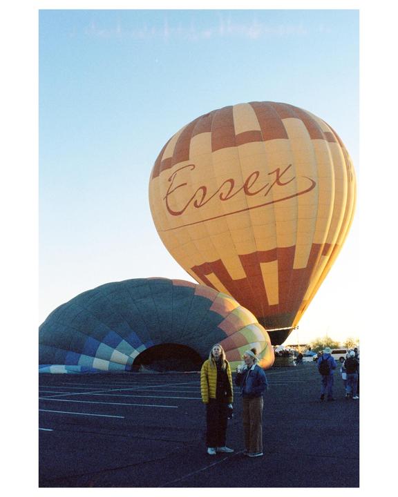 Two women stand in a parking lot next to two hot air balloons, one of which is partially deflated.