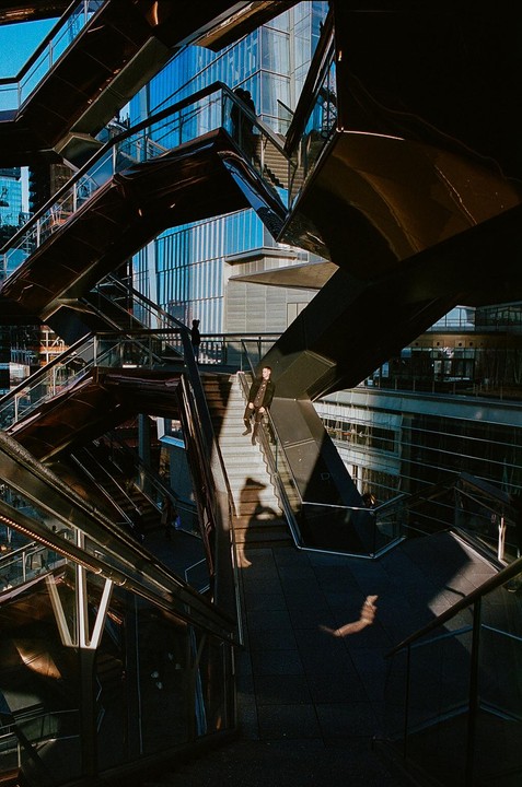 A man sits on a staircase in a modern building with many intersecting staircases and glass walls.