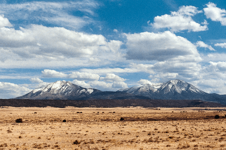 A vast, dry plain stretches towards snow-capped mountains under a blue sky with white clouds.