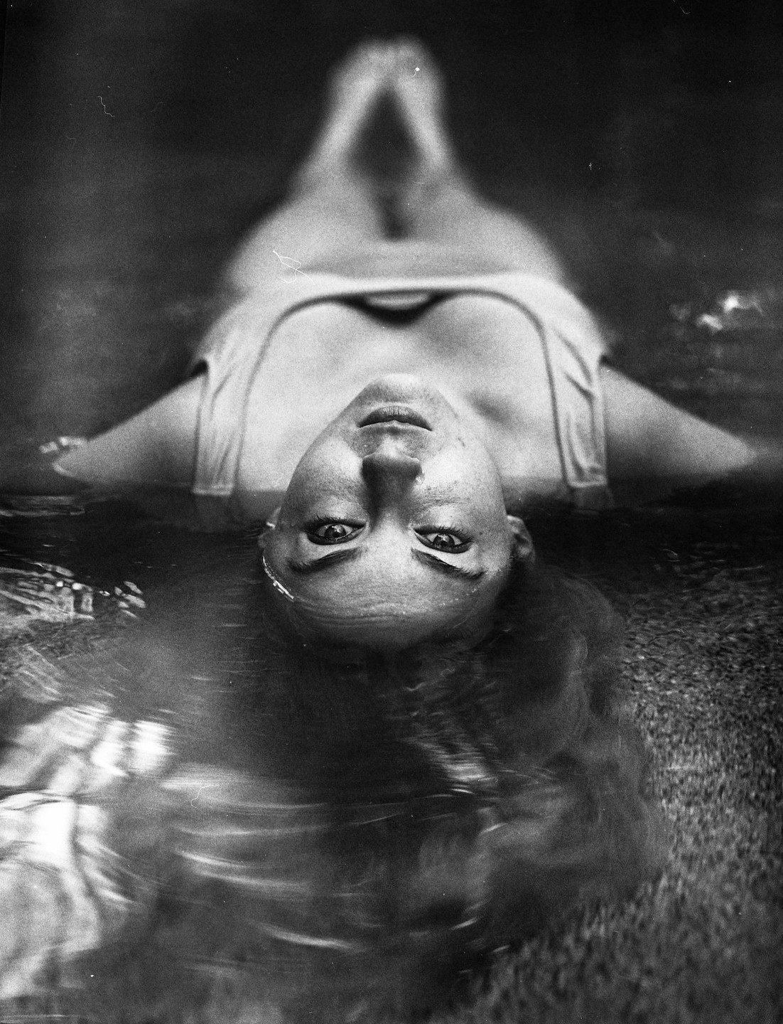 A woman floats on her back in water, looking up at the viewer.