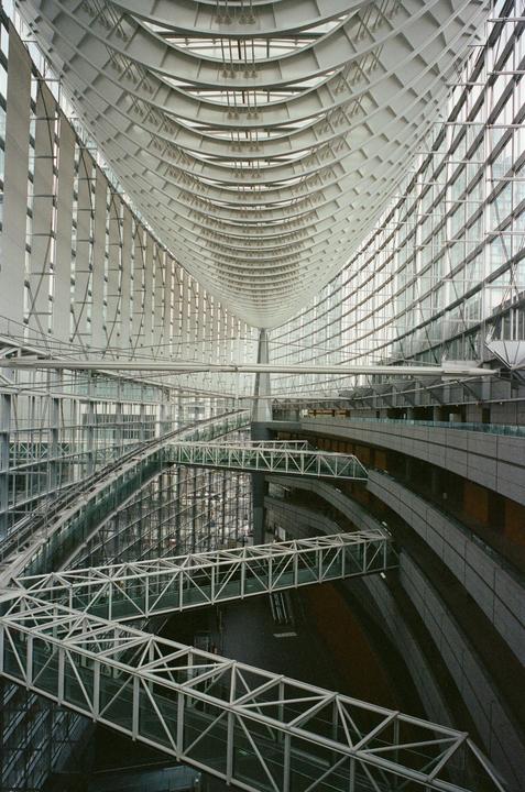 A large, modern building interior features multiple levels of walkways and a high, arched ceiling.