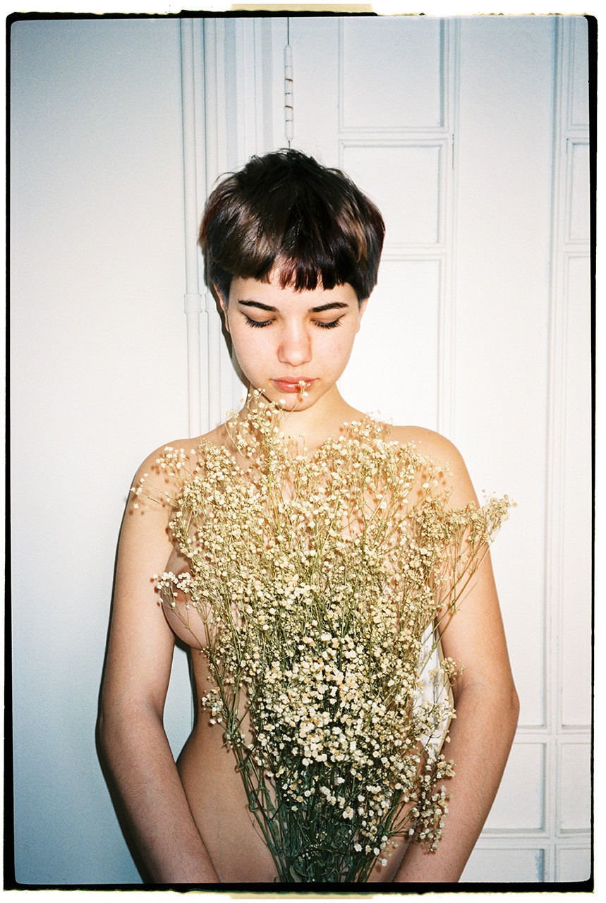 A woman with short hair holds a large bouquet of baby's breath flowers in front of her body.