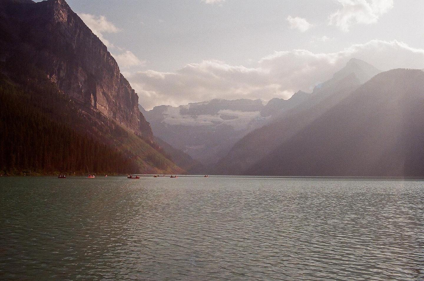 A wide shot shows a lake with several small boats and mountains in the background under a cloudy sky.