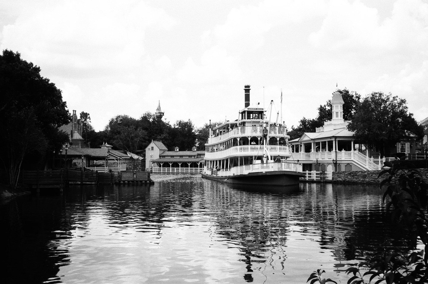 A large paddle boat is docked at a pier next to several buildings and trees.