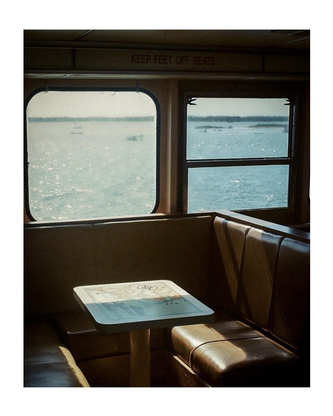 The interior of a boat with a table and seats looks out onto a body of water.