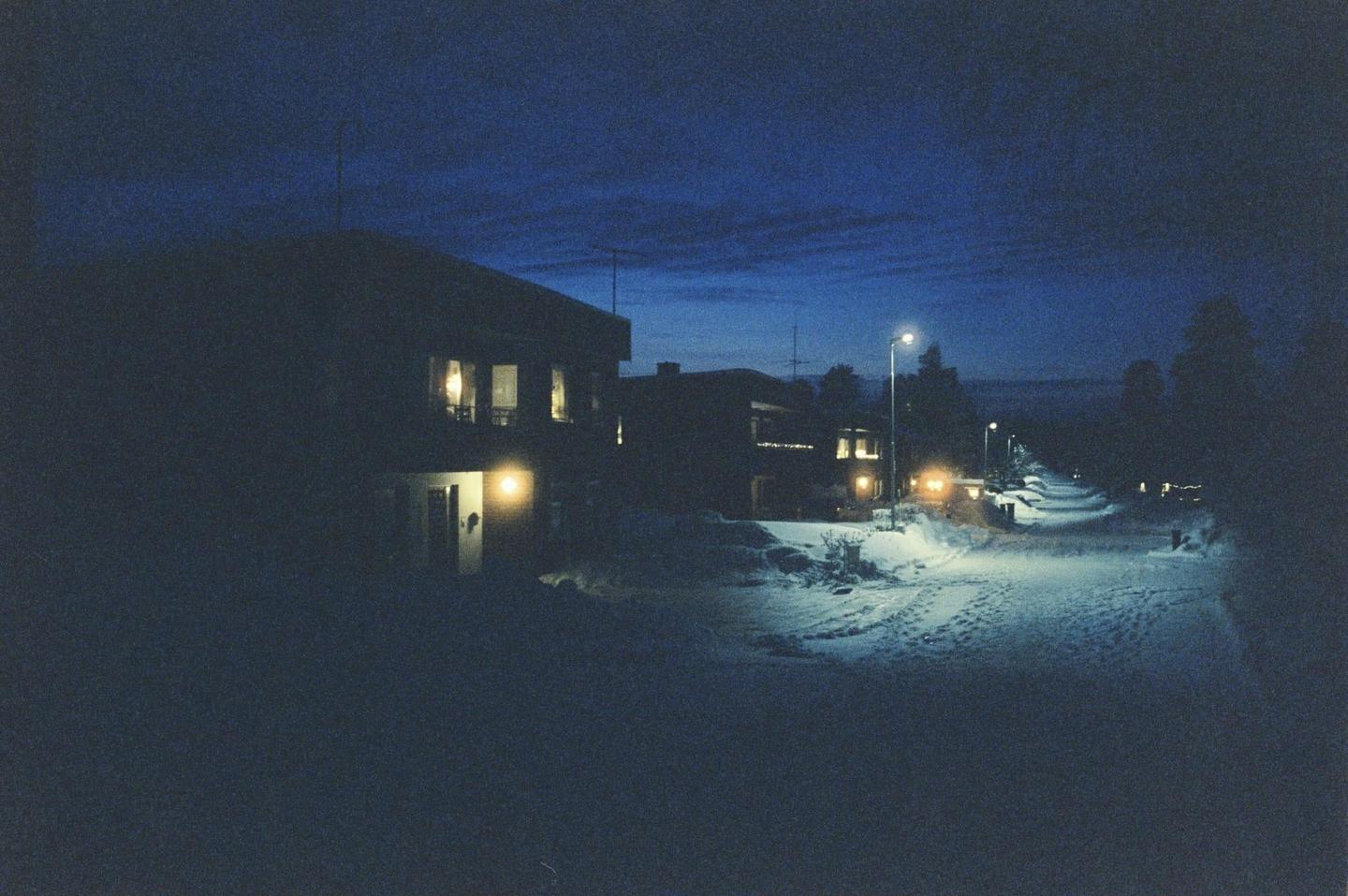 A snow-covered street with houses and streetlights is visible at night.