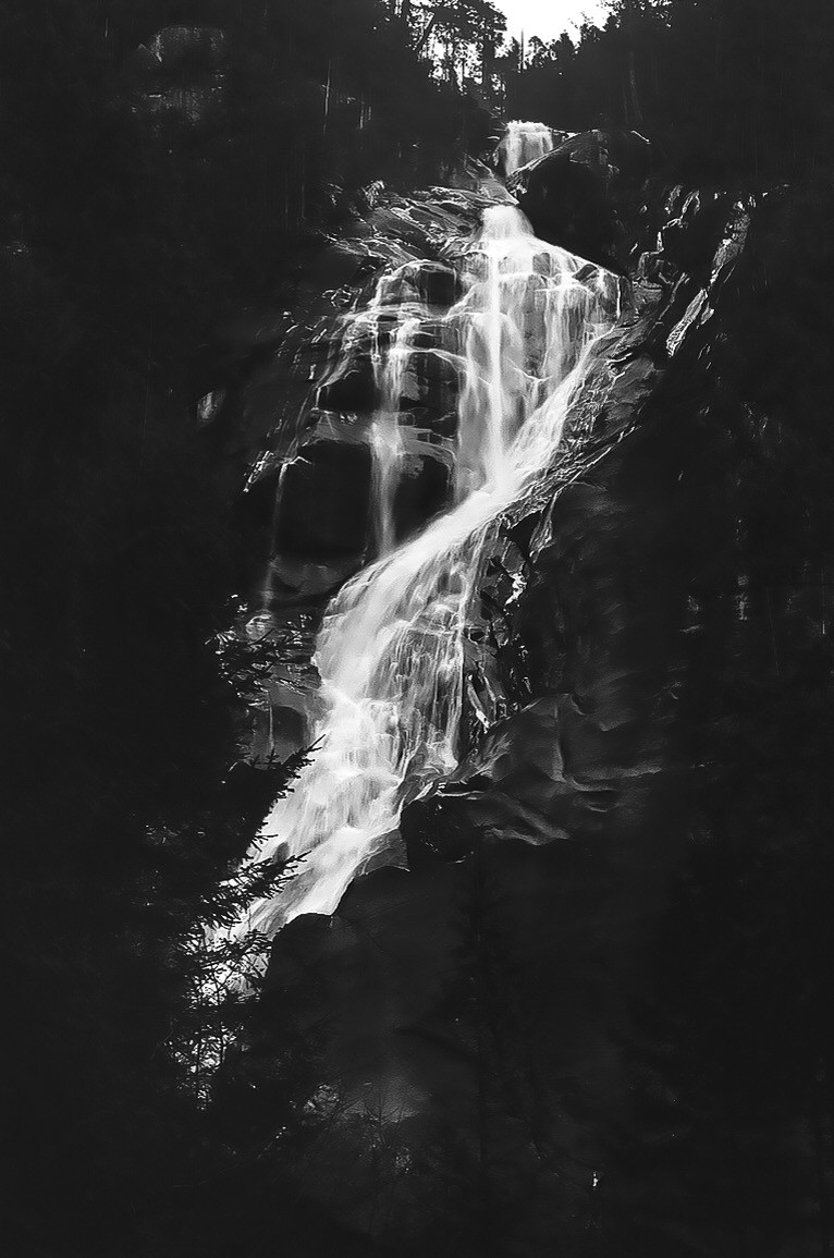 A long exposure shot captures a waterfall cascading down a dark, rocky cliff face surrounded by trees.