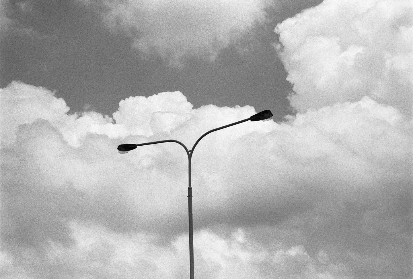 A street light with two lamps stands against a cloudy sky.