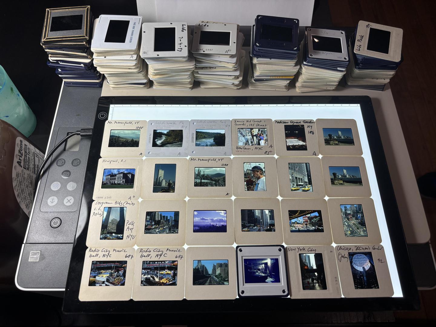 A collection of film slides are arranged on a light table, with stacks of additional slides visible in the background.