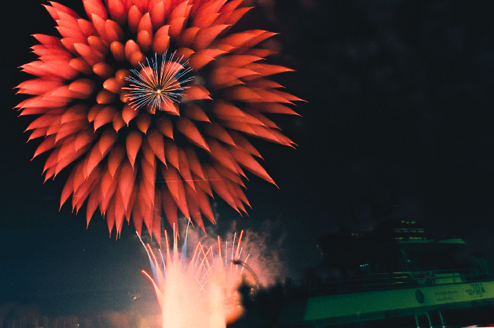 Red fireworks explode in the night sky above a boat.