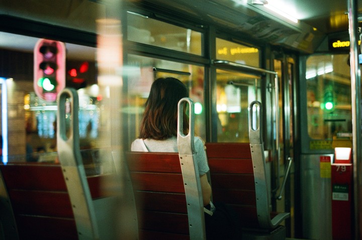 A woman sits on a bus at night, looking out the window at the city lights.
