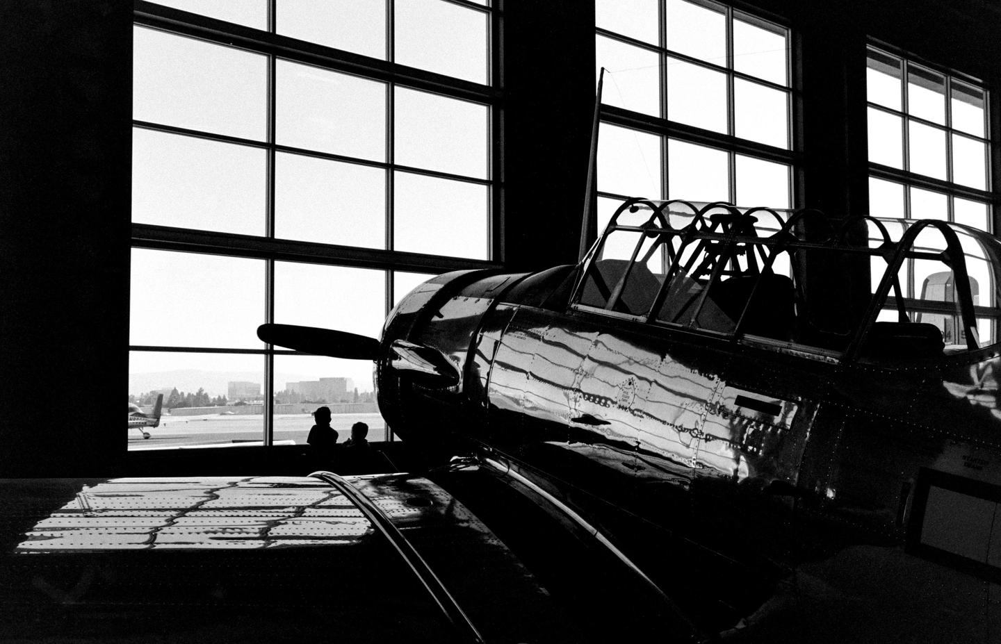 A shiny airplane is parked inside a hangar with large windows looking out onto an airfield.