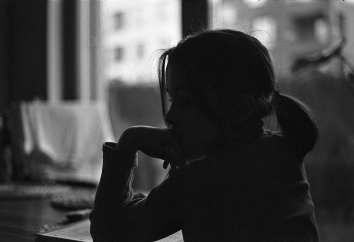 A child sits in profile with their arm resting on a table, silhouetted against a window.