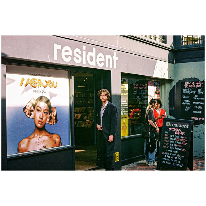 A man stands in the doorway of a record store next to a large album advertisement.