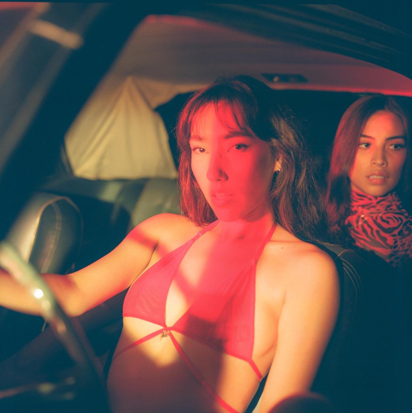 Two women are sitting in a car with red light illuminating the interior.