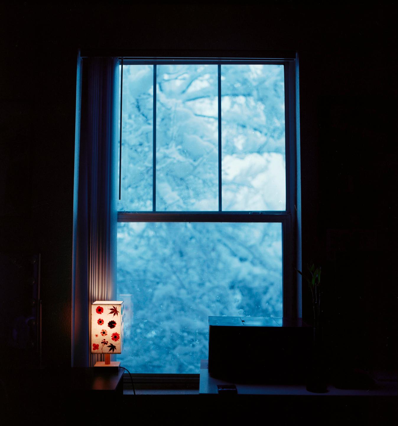 A window looks out onto a snowy landscape, with a small lamp on the windowsill.