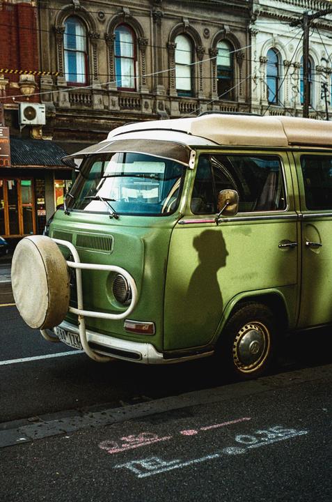 A green van is parked on a street with a shadow of a person on its side.