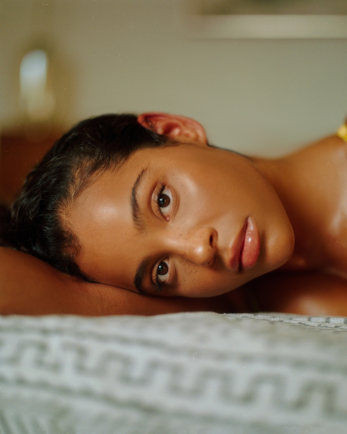 A woman with dark hair and freckles lies on a textured blanket, looking directly at the viewer.