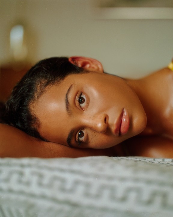 A woman with dark hair and freckles lies on a textured blanket, looking directly at the viewer.