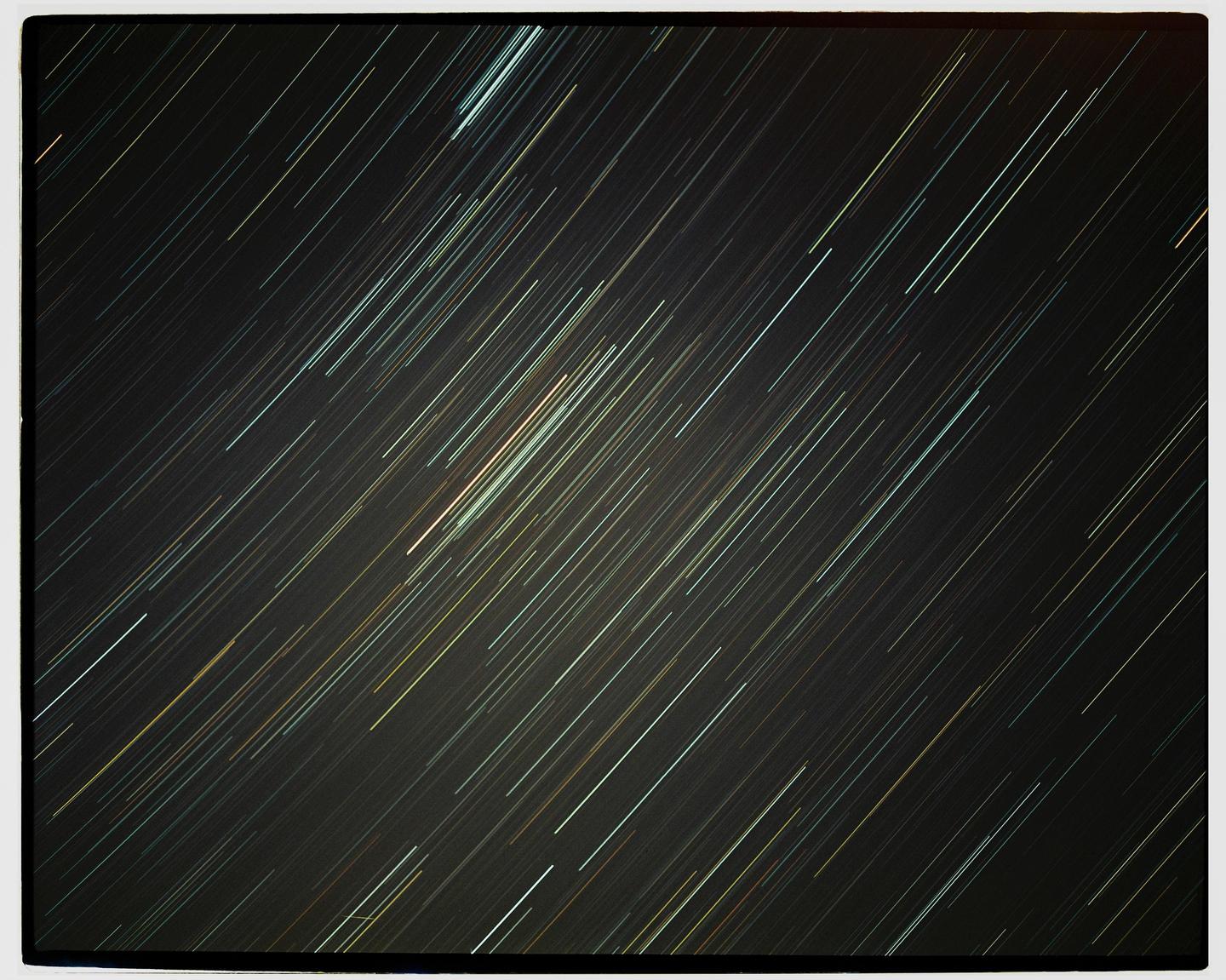 A long exposure photograph captures the movement of stars across a dark night sky, creating streaks of light.