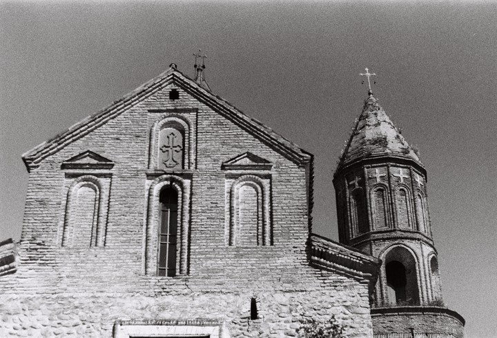 A brick church with a tall, conical tower stands against a clear sky.