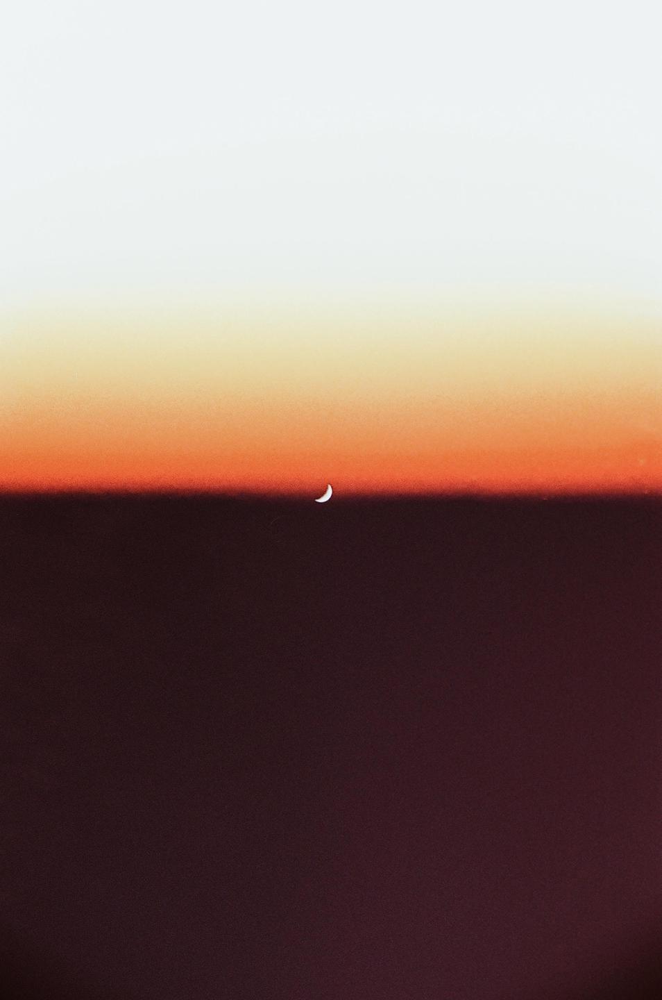 A crescent moon is visible in a gradient sky of white, orange, and dark red.
