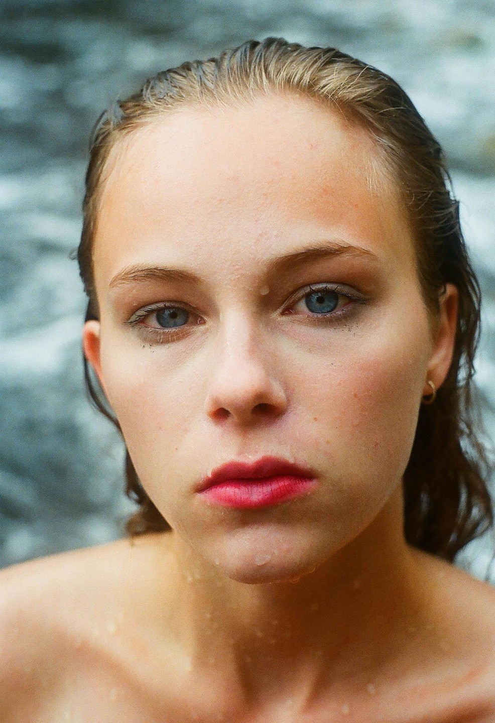 A woman with wet hair and water droplets on her face looks directly at the viewer.