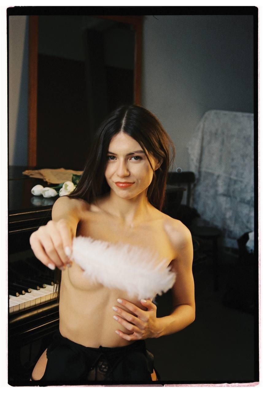 A woman holds a white feather in front of her chest while sitting at a piano.
