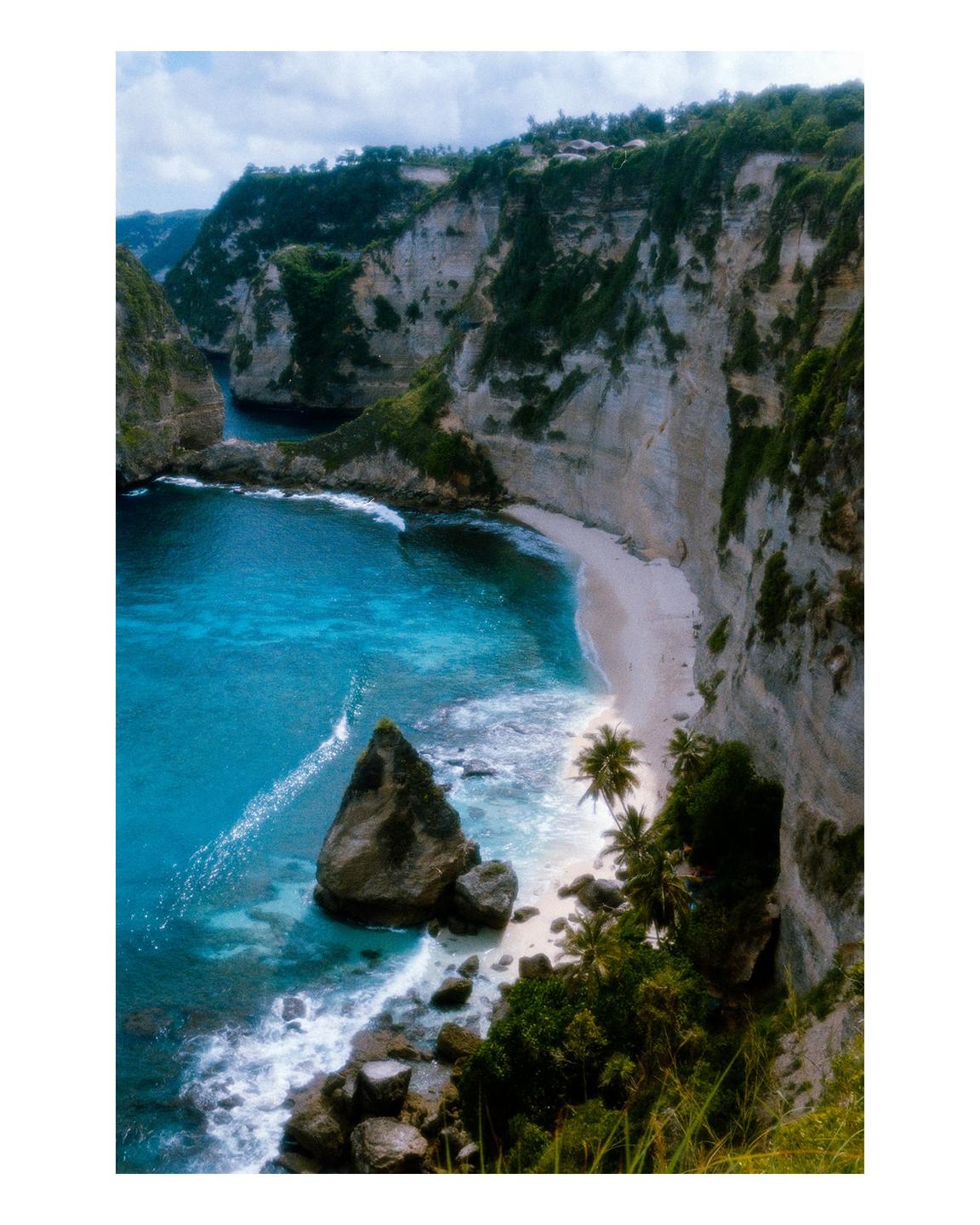 A secluded beach with turquoise water is nestled between towering cliffs covered in lush vegetation.