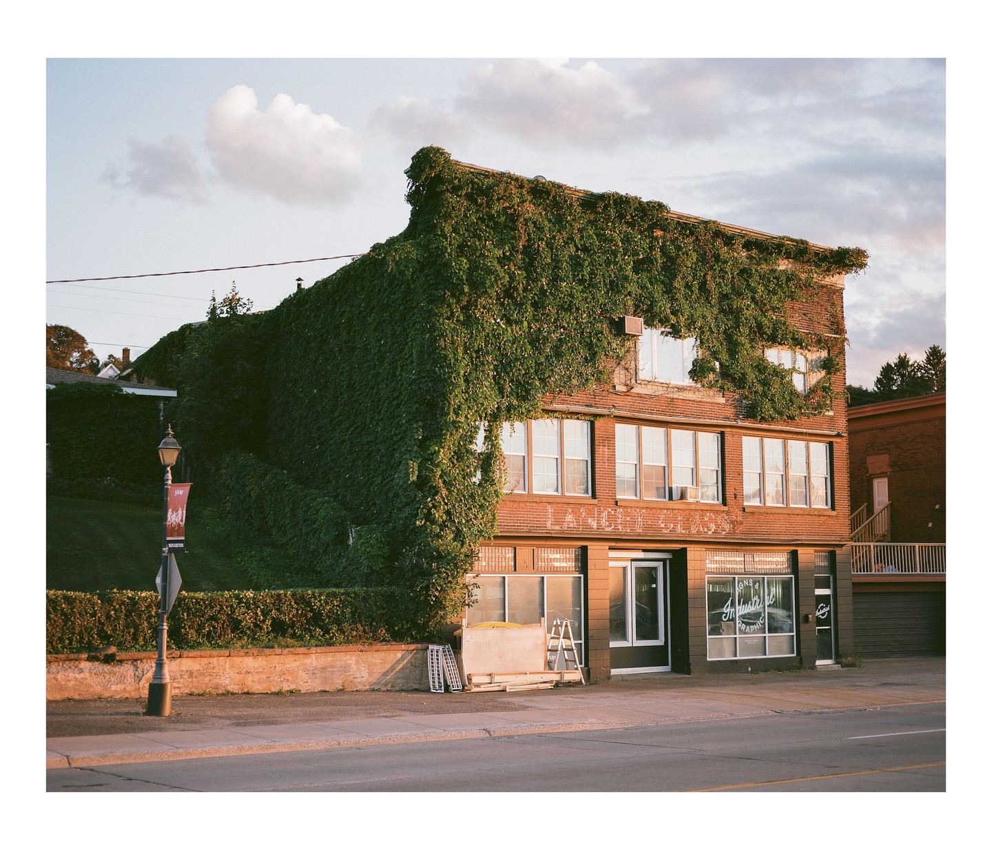 A brick building covered in ivy stands next to a street under a cloudy sky.