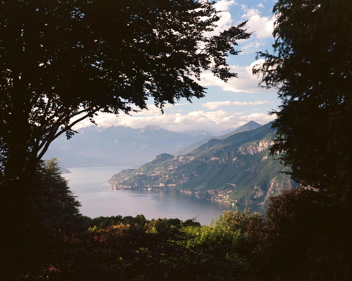 A large lake is surrounded by mountains and trees under a cloudy sky.