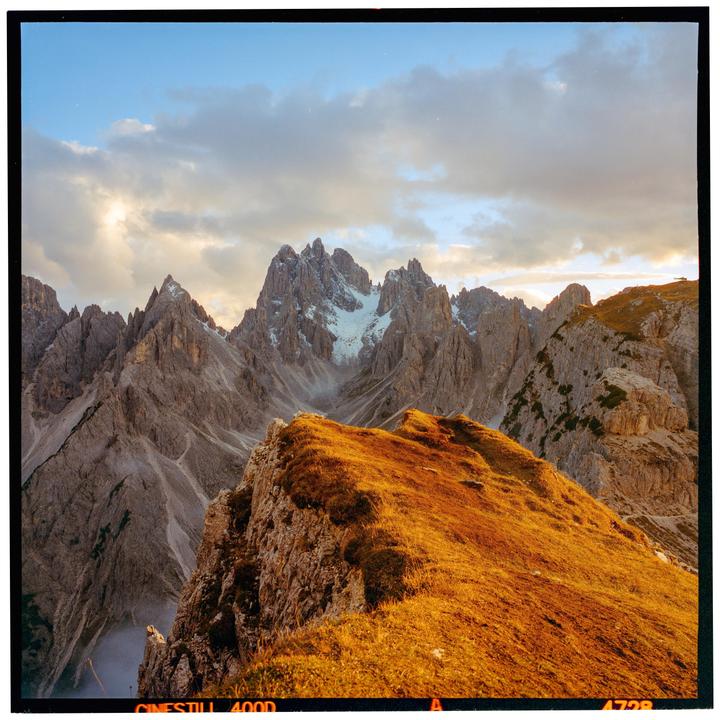 A mountain range with snow-capped peaks is visible under a cloudy sky, with a sunlit ridge in the foreground.