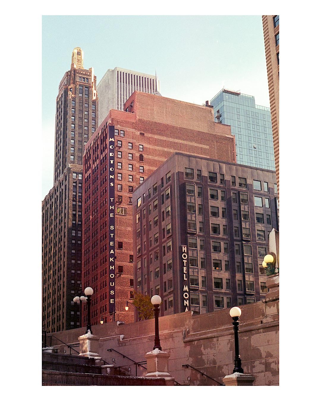 A low angle view shows several tall buildings in a city, with streetlights and stairs in the foreground.