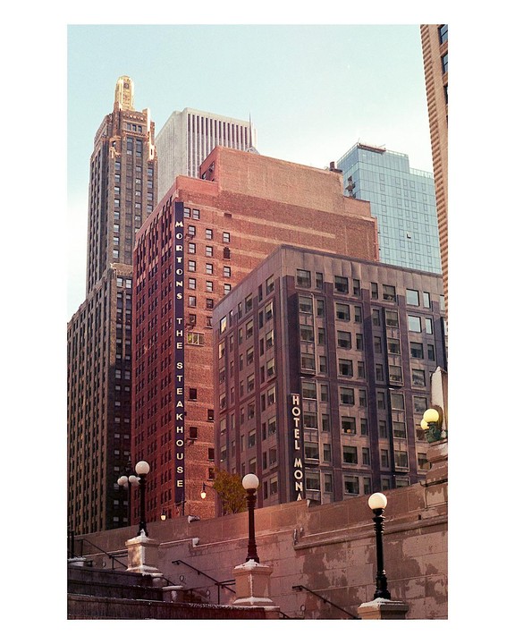 A low angle view shows several tall buildings in a city, with streetlights and stairs in the foreground.