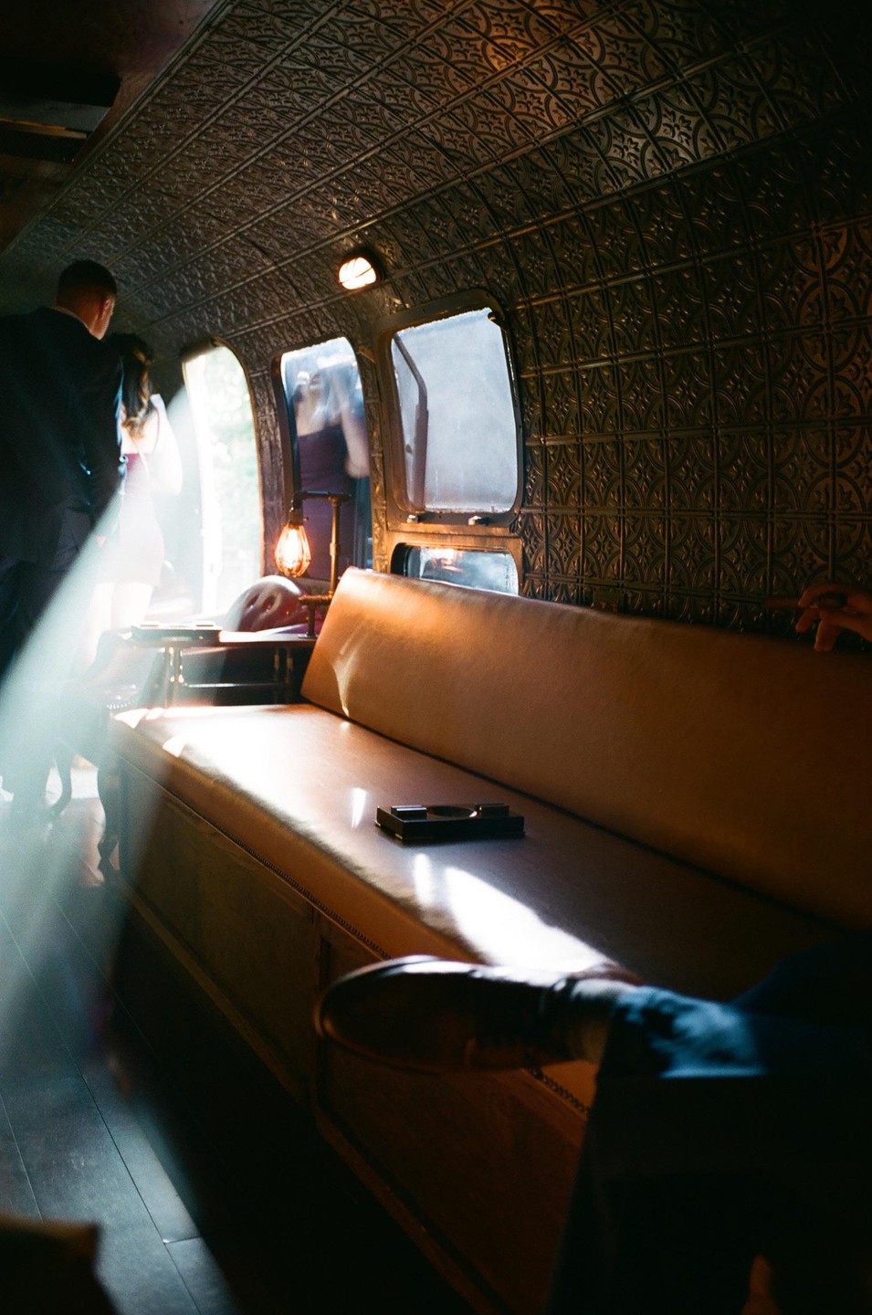 A couple stands near a window in a vintage vehicle with a long leather bench seat and ornate ceiling.