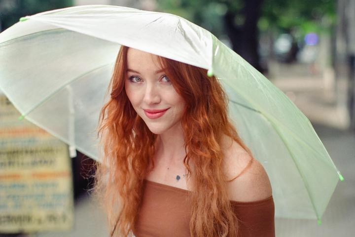 A woman with long red hair looks out from under a light green umbrella.