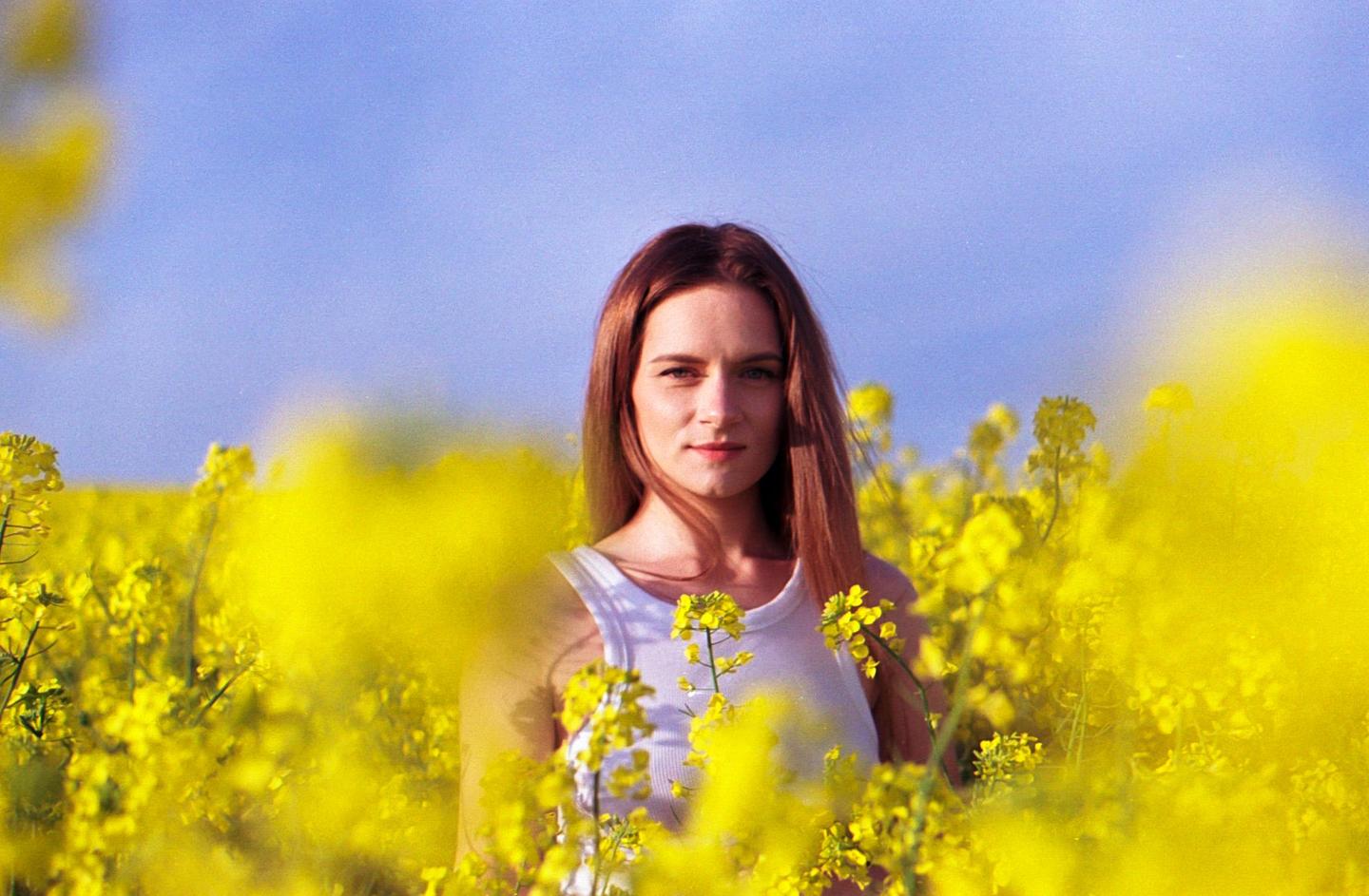 A woman stands in a field of yellow flowers under a blue sky.